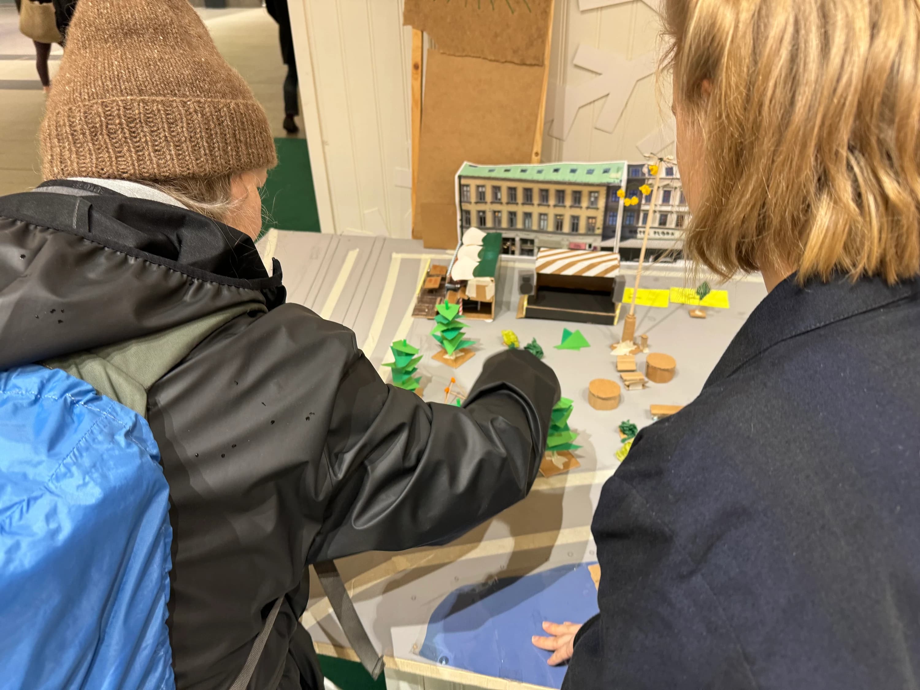 Two people leaning over the model in Nordstan, one reaching in to move a piece, the other resting a hand on the board.