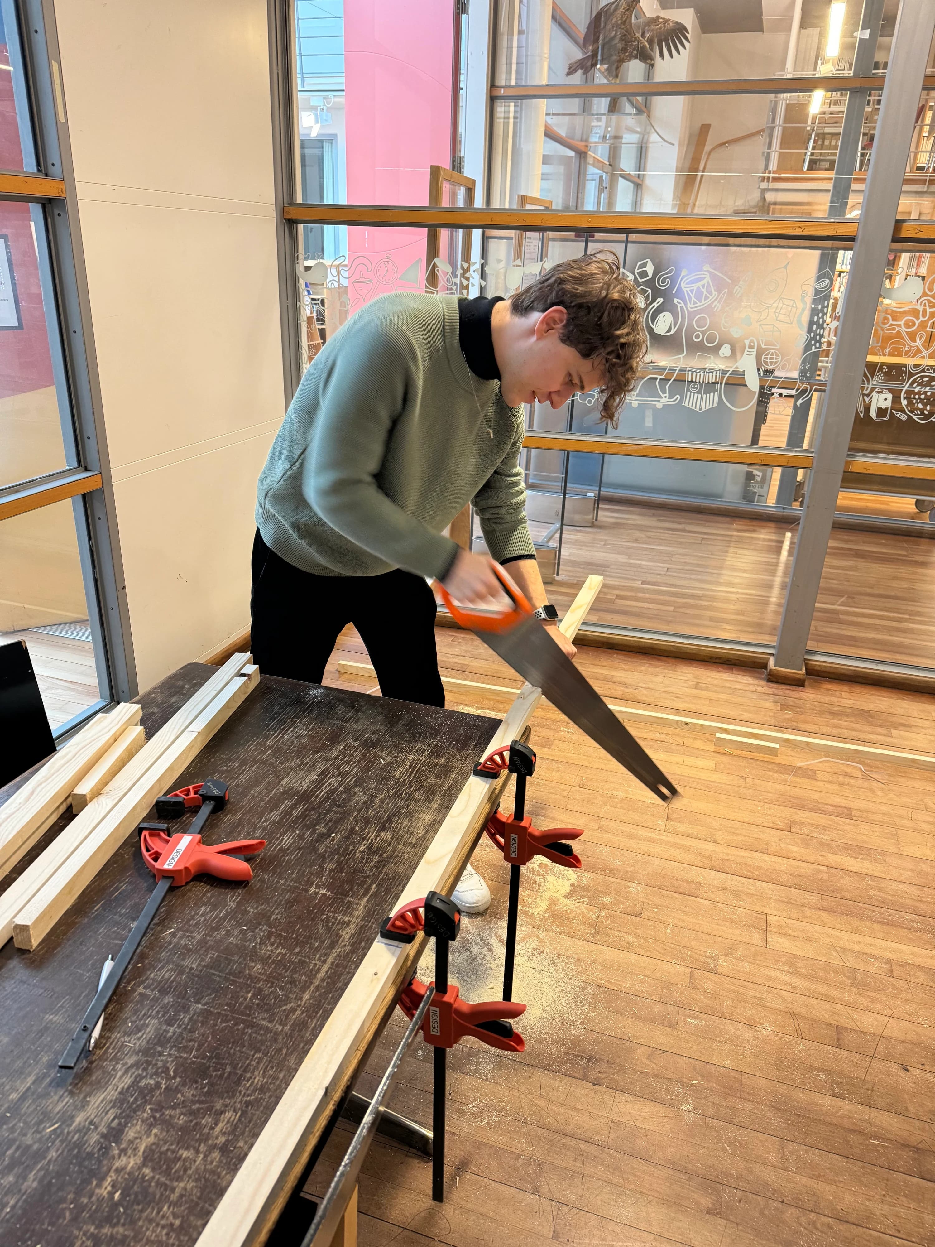 Sawing a length of timber clamped to a workbench in the HDK-Valand workshop, building the table the model sits on.
