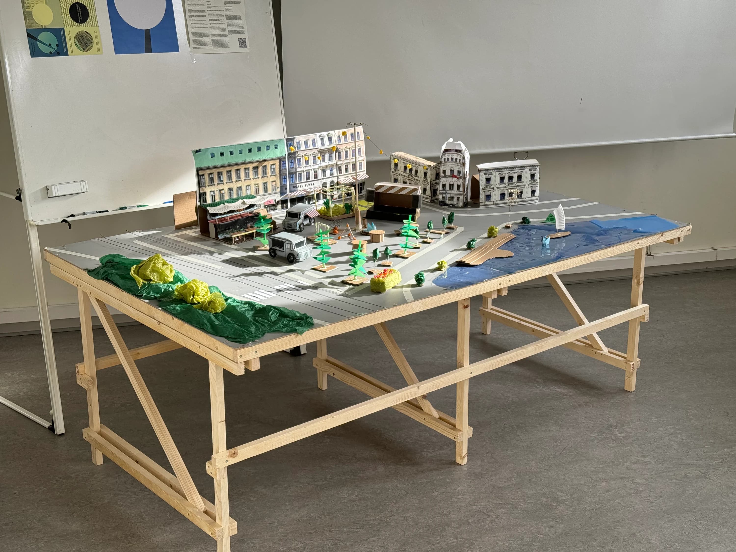 The finished model on a purpose-built wooden trestle table: a grey board with the square's road markings, paper facades of the surrounding buildings, market stalls, trees and a canal.