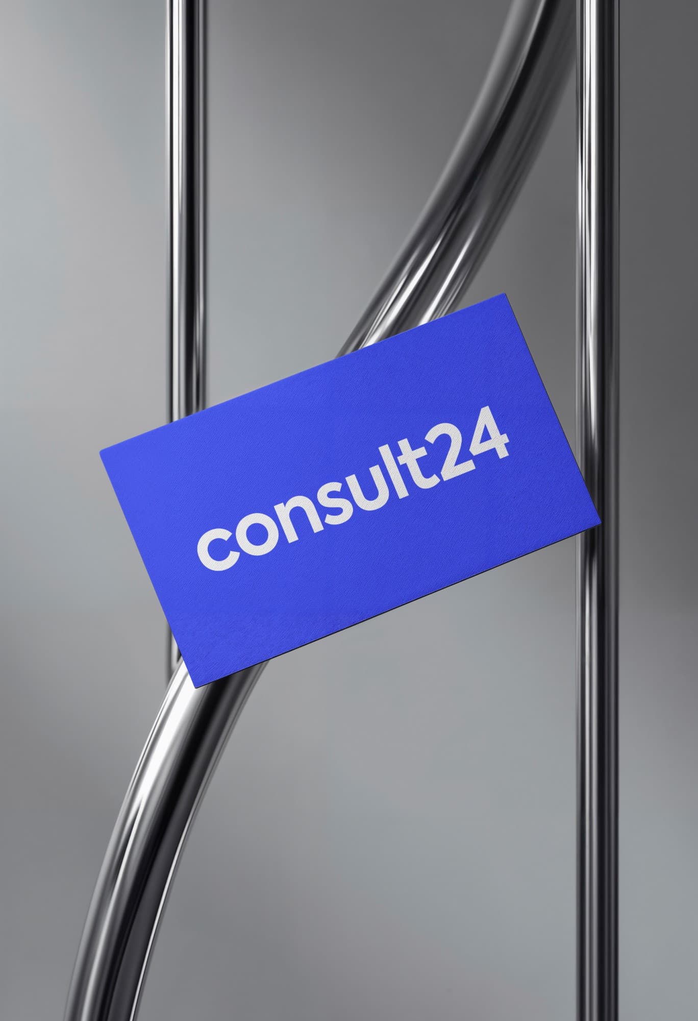 A blue consult24 business card with the wordmark in white, resting between polished steel tubes.