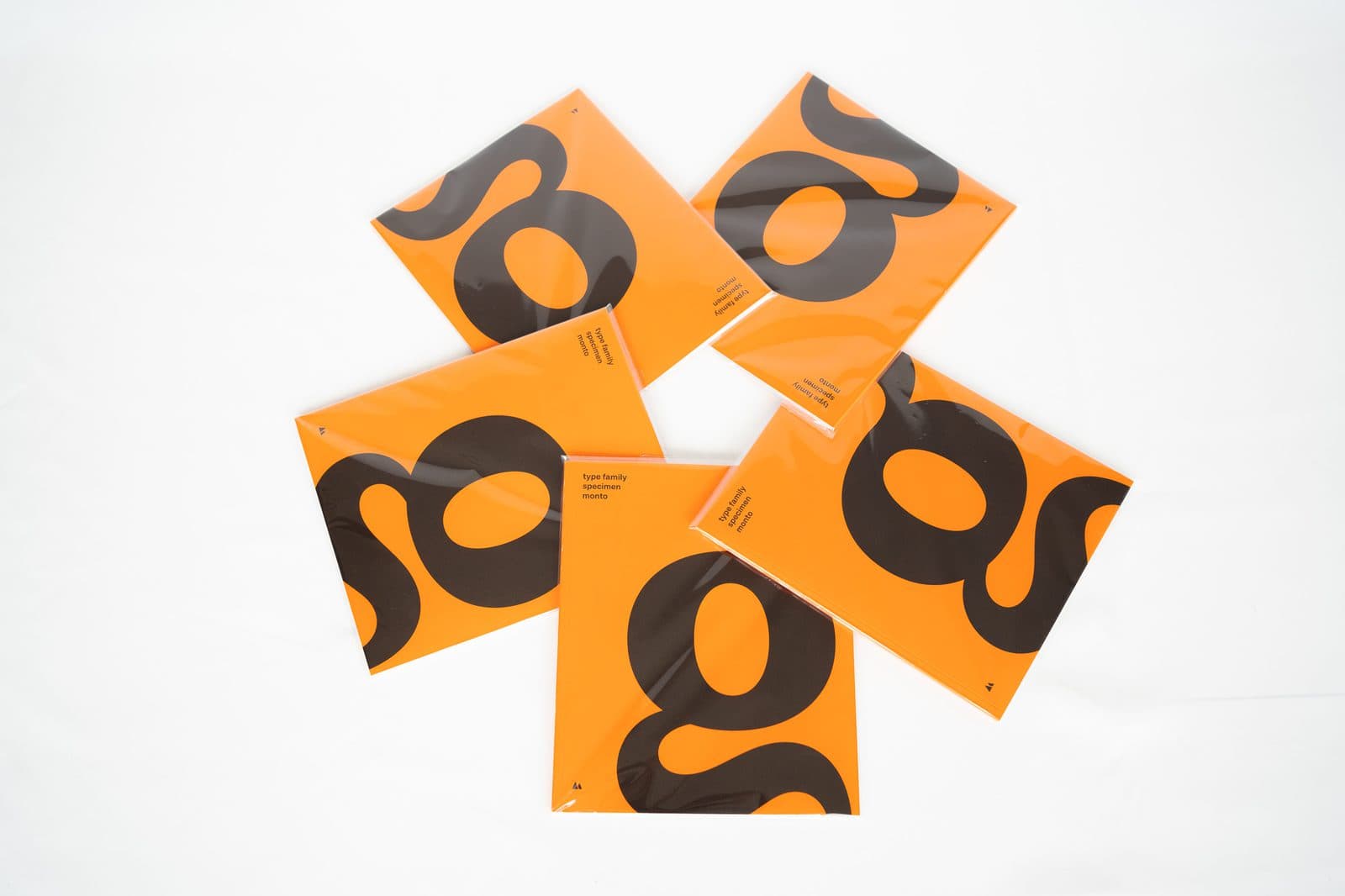 Five orange type specimens fanned out on white, each cover filled by a large black lowercase g.